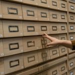 A person organizing wooden drawers in an archive room with a focus on storage.