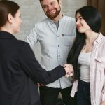 Three adults shaking hands in a professional meeting setting, showing agreement and positive interaction.