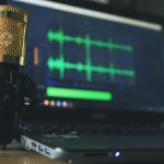 Close-up of a golden microphone and laptop used for audio editing.